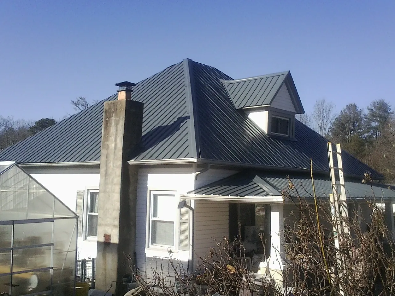 Dark blue standing seam metal roof on a white farmhouse with dormer — Slate & Tile Roof Repair by Roofing Brothers in Cedar Creek