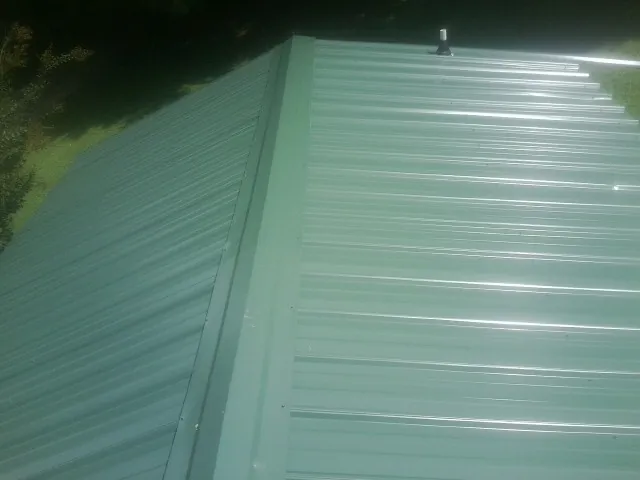 New green metal panels meeting at the ridge of a roof — Flat Roof Repair work by our crew in Cedar Creek