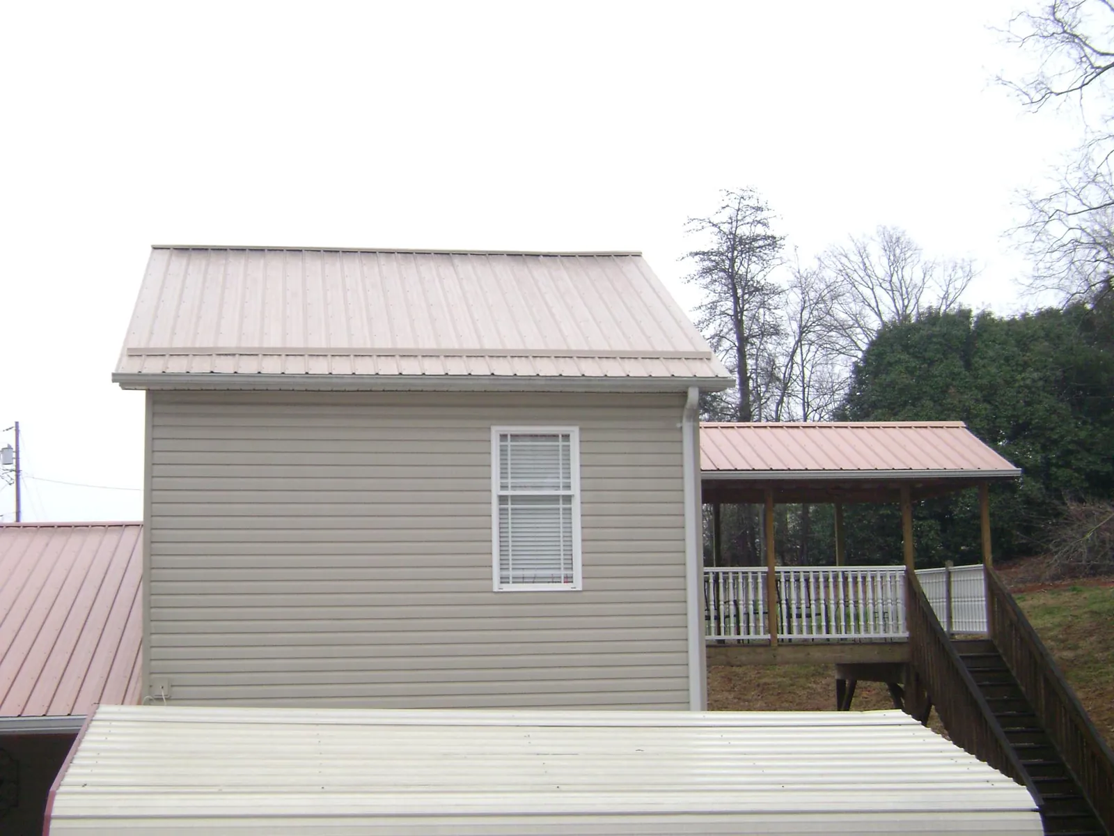 Tan metal roofs on a two story addition and attached porch, from a Roof Replacement job in Cedar Creek