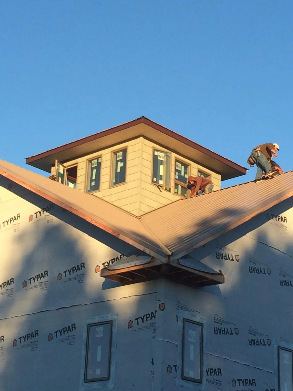 Roofers working around a rooftop cupola on a new metal roof at sunset — Roof Waterproofing in Cedar Creek by Roofing Brothers